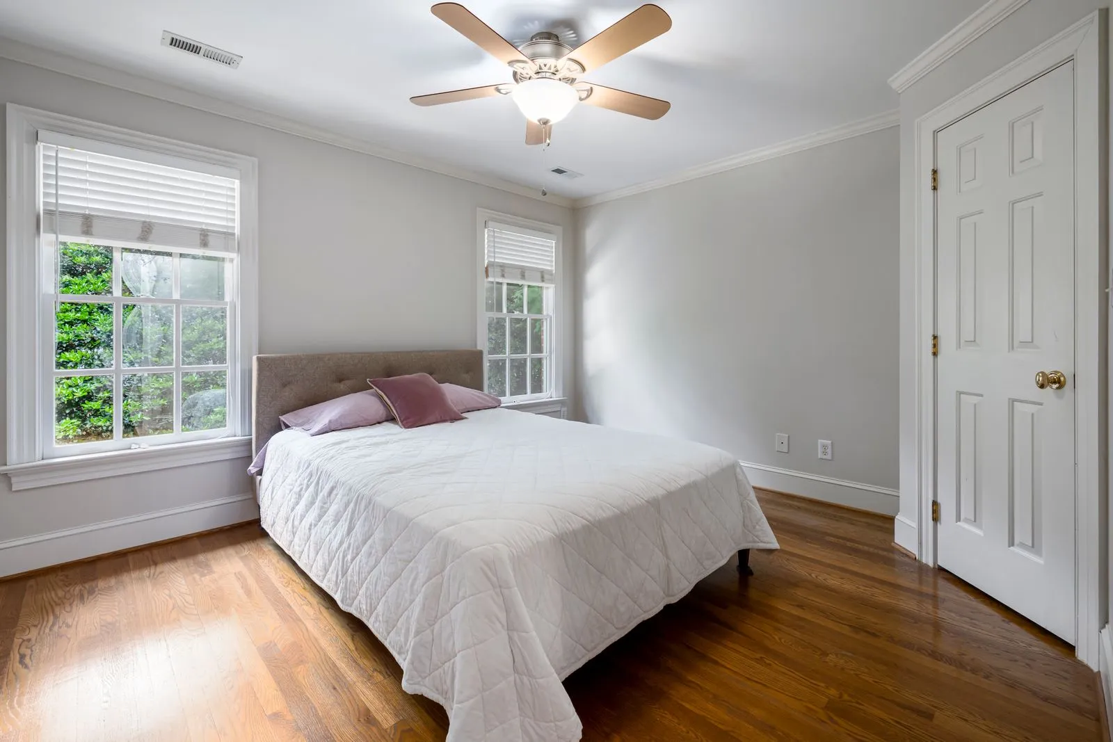 A freshly made bed in a sunlit Florida bedroom, greenery outside the windows